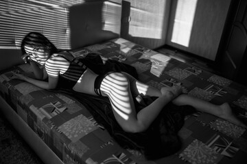 Gorgeous slim woman lies on the bed and relaxes under sun rays. Black and white snapshot of an attractive lady.