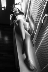 Black and white fashion photo of a slim sexual woman on the windowsill under sun light. Female sexuality, woman's silhouette, natural beauty of a slender girl in the black underwear.