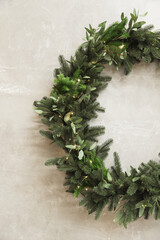 Christmas wreath made of fir branches hanging on a gray wall. Half wreath