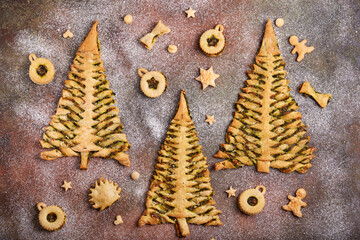 Christmas tree shape puff pastry pies with spinach, garlic and cheese, and puff pastry Linzer Christmas tree toys. Delicious homemade New Year savory baking. 