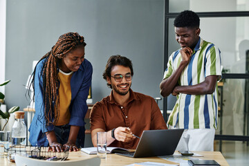 Young successful designer pointing at laptop screen during discussion of new creative project with...