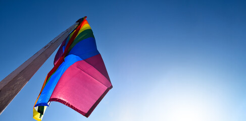 Rainbow flag, LGBT simbol, holding in hands of boy against clear bluesky background, soft and  selective focus, concept for LGBT celebration in pride month, June, around the world, copy space.