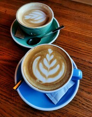 Top view of lattes in blue and green cups on a wooden table.
