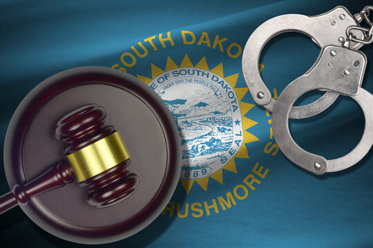 South Dakota US state flag with judge mallet and handcuffs in dark room. Concept of criminal and punishment