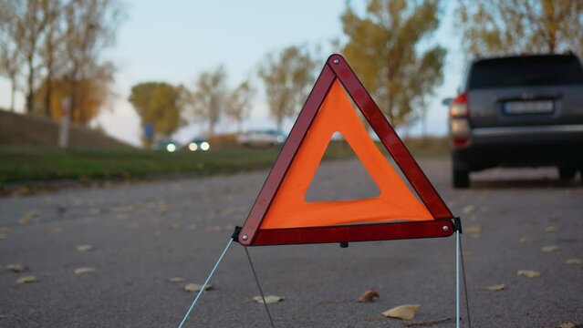 Reflecting warning triangle on road behind broken car, pickup passing in other direction. Emergency stop sing on side of road