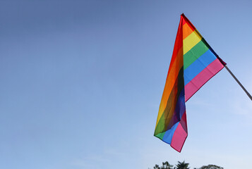 Look up view of rainbow LGBT flag waving in the blue sky background, soft and selective focus, copy space. To celebrate LGBT communities in pride month                               
