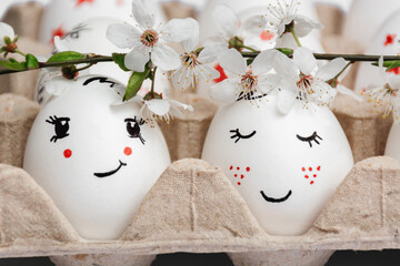 Close-up of delicately painted Easter eggs in paper eco-friendly tray. From above, sprig of spring white flowers from fruit trees. Pair of eggs looks like bride and groom. Spring style. Postcard