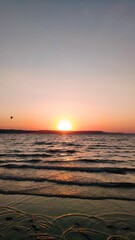 Bright sun shining in orange and blue sunset sky over the water seen from the shore