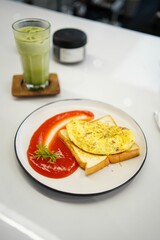 Vertical shot of a gourmet omelette and toast on a dish with ketchup near a matcha drink