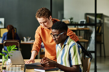 Two young managers or designers in casualwear looking at laptop screen while preparing for...