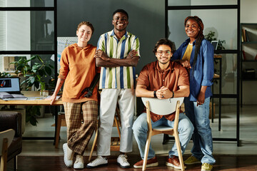 Group of young multicultural colleagues in casualwear standing against workplace in office and...