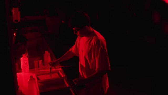 Caucasian young man developing analog photography in a dark roo