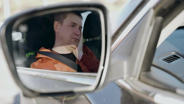 Tired sleepy driver rubs his eyes, wants to sleep. View through the side mirror of a car. Transport security.