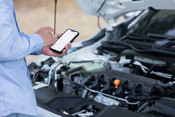 Mechanic checks engine oil level and uses online smartphone check service data in a car garage or auto repair service center.