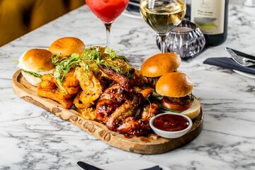 Appetizing shot of a wooden tray with roasted chicken wings,tiny burgers ketchup over a marble table