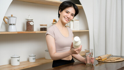 An Asian young woman in sportswear drinking milk in kitchen at home , healthy lifestyle concept