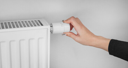 A woman turns the regulator of the thermostatic radiator valve to the middle position to set the...