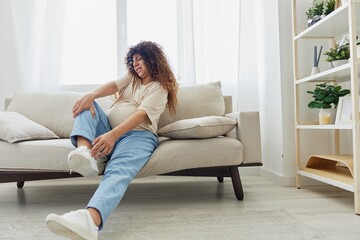 Pregnant woman sitting on the couch at home and wearing comfortable shoes for pregnancy with a problem due to the stomach, headache, pregnancy and motherhood difficulties, severe fatigue