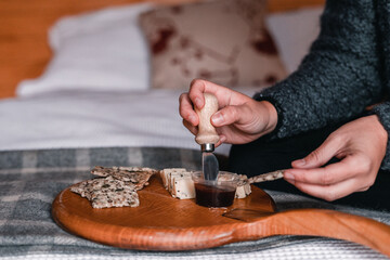 Fototapeta na wymiar hands of caucasian girl spreading with a wooden and metal knife dark barbecue sauce on a small thin appetizing cereal toast on a small wooden board on a bed