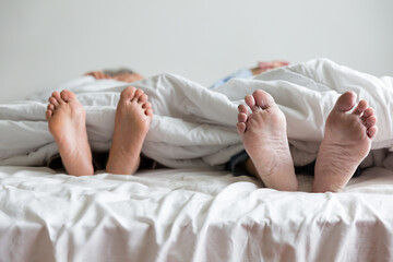 Elderly couple's feet sticking out from under the blanket during sleeping on bed together in...