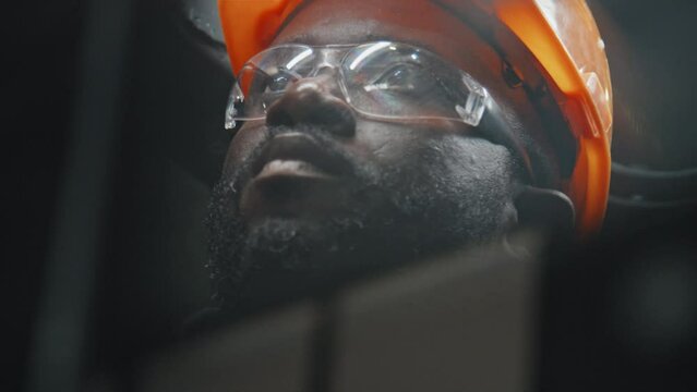 Close up of African American man in hard hat connecting wires while working at industrial factory