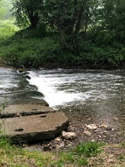 Vertical shot of a river flowing in a forest down the rocks surrounded by wild green nature