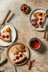 Pieces of The New York Times Plum Cake pie sprinkled with powdered sugar for tea on brown textured background, autumn tea party concept, top view
