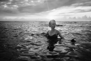 Black and white snapshot of a beautiful woman in the ocean. Dark portrait of a sensual gentle girl in the water in summer. Brunette woman is swimming and relaxing in the water before sunset. 