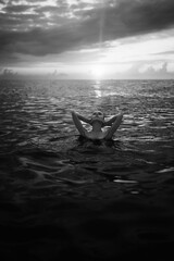 Black and white snapshot of a beautiful woman in the ocean. Dark portrait of a sensual gentle girl in the water in summer. Brunette woman is swimming and relaxing in the water before sunset. 