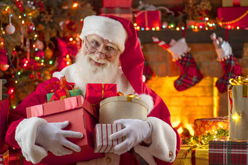 Santa Claus with gift box presents near fireplace and Christmas tree. Festive interior inside...