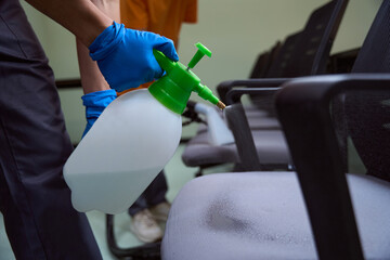 Professional cleaning company worker spray-disinfecting chairs with chemicals