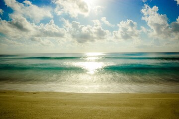 Blauwe oceaan met een zandstrand en zonlicht weerspiegeld in de wateren onder de blauwe lucht