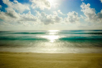Wall murals Reflection Blue ocean with a sandy beach and sunlight reflected in the waters under blue sky