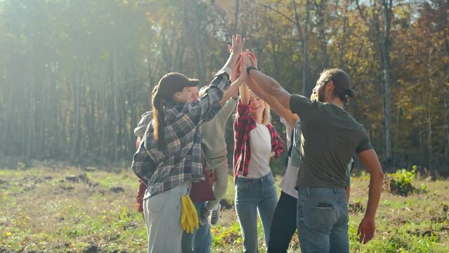 Caucasian team of males and females, volunteers with child giving high five in circle as gesture of cooperation and friendship. Successful coworking together concept. Eco activists. Outdoor.