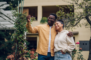 Multiracial couple holding keys and standing outside their new home