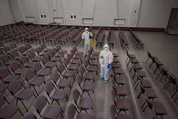 Janitors in protective suits preparing for disinfective fogging of building