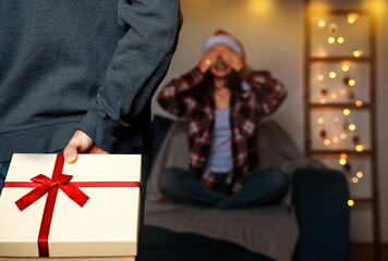 People giving christmas presents, gift box in hand defocused person in background.