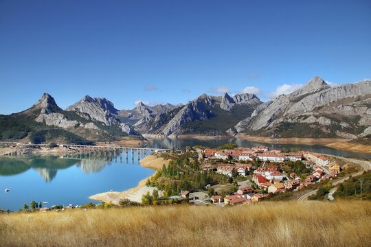 Awesome shot of a small village by the river, mountains in background in Riano reservoir Leon Spain