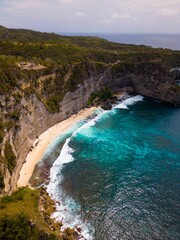 Vertical aerial of Suwehan beach with rocky and forested cliffs around and a cloudy sky background