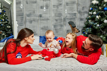 Young family on the bed with children on the background of the Christmas tree