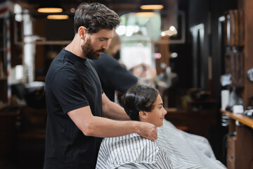 Side view of hairdresser wearing hairdressing cape on teen client in beauty salon.