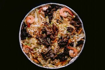 Closeup shot of a dish in an aluminum foil bowl, made of cabbage and shrimps,on a black background