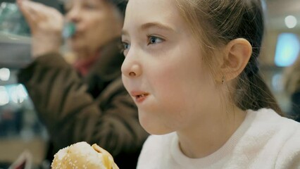 Beautiful girl eating burger in shopping mall enjoying delicious juicy hamburger mouth watering meal with meat and cheese. Street fast food for lunch dinner and breakfast. Relevance of healthy eating