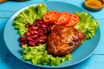 Chicken with red beans garnished with tomato on lettuce leaves in a blue plate on a blue wooden table.