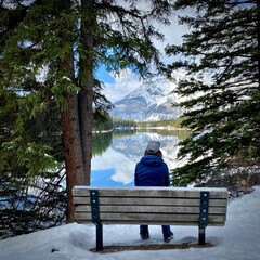 person sitting on a bench by lake and mountains