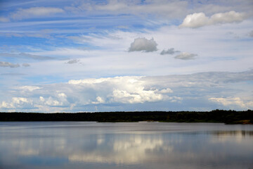 July. Blue sky and white clouds. Forest lake and reflection in the water. The banks of the reservoir, 