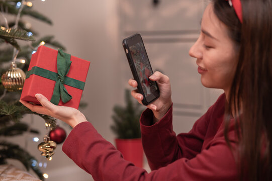 Selective focus on hand of young Asian woman using smartphone taking photo of new year Christmas present box before send or received from friend or family during Christmas festival celebration.