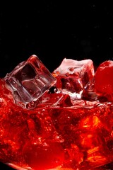 Vertical shot of cherries splashing into a drink filled with ice in a glass cup on black background