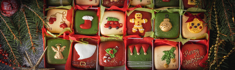 Delicious Christmas cookies set in a gift box. Advent calendar to count the days in anticipation of Christmas. Gingerbread cookies with festive red and green icing on the Christmas panorama background