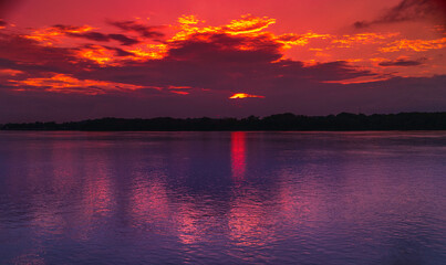 Sunset over the Mississippi River with glowing red and orange clouds and purple, pink water reflections